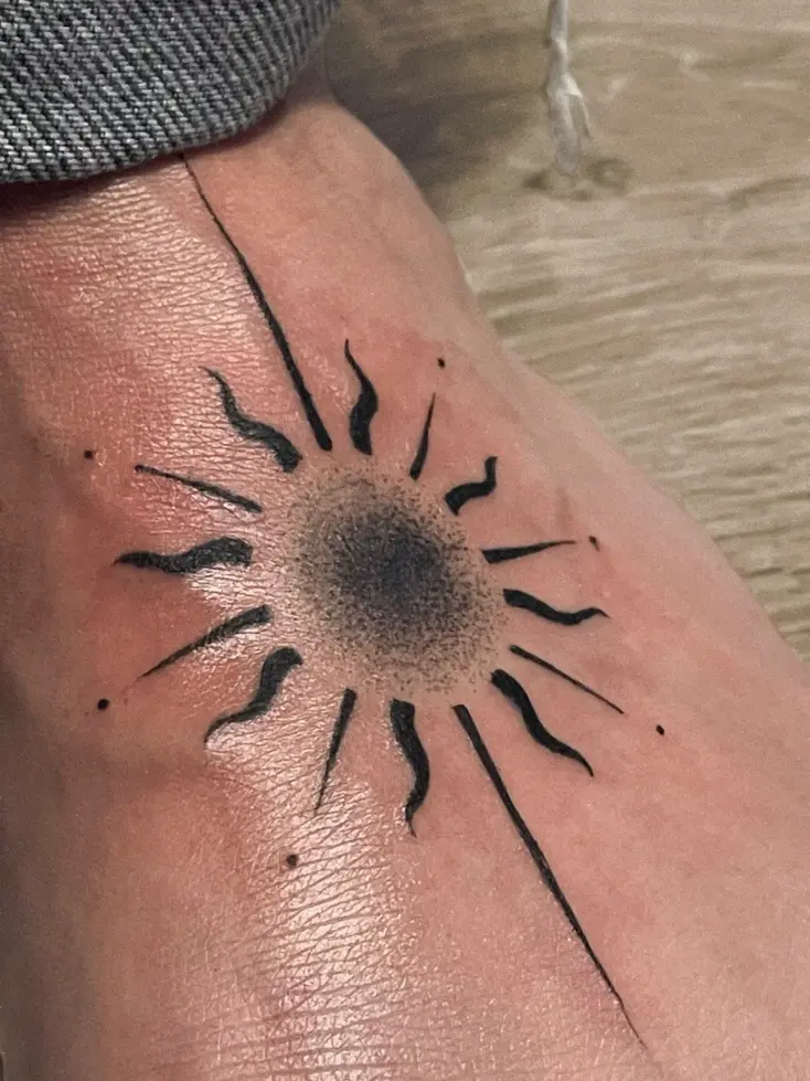 Tatuaje blackwork de un sol con rayos en el dorso de la mano
