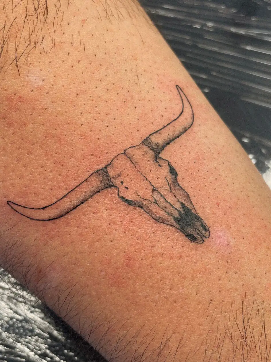 Tatuaje fine line de un cráneo de toro con cuernos en el brazo