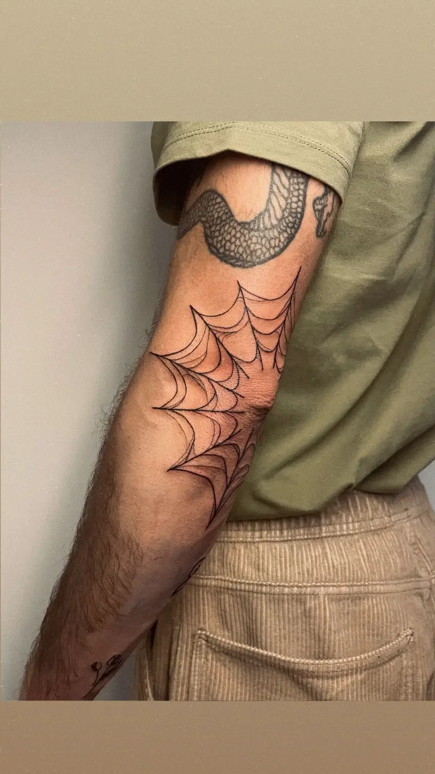 Tatuaje de telaraña que cubre el codo y baja por el antebrazo